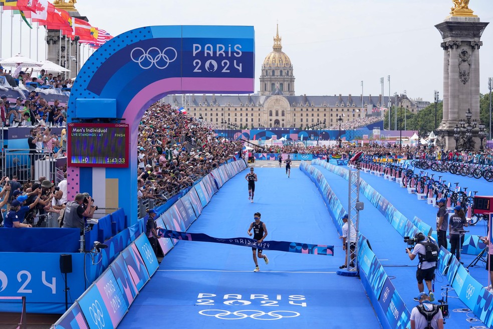 O triatleta britânico Alex Yee cruzando a linha de chegada em frente a uma multidão lotada nos Jogos Olímpicos de Paris 2024 — Foto: Nathan Laine/Bloomberg