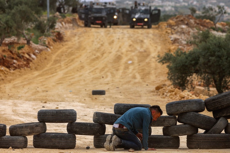 Manifestante palestino se agacha atrás de barricada enquanto forças israelenses se aproximam do povoado de Beita, na Cisjordânia ocupada, para reprimir protestos contra a expansão de assentamentos