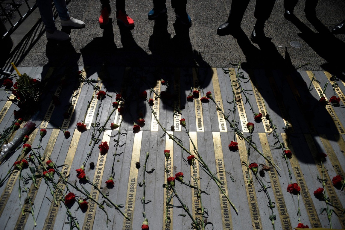 Pessoas observam um memorial com os nomes das vítimas da ditadura chilena — Foto: Pablo Vera / AFP