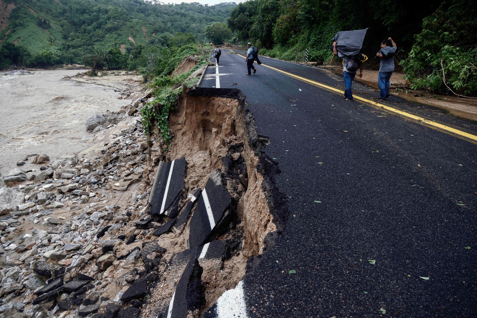 TOPSHOT - Pessoas passam por trecho de estrada que foi arrastado na comunidade Kilometro 42, próximo a Acapulco, estado de Guerrero, México, após a passagem do furacão Otis — Foto: RODRIGO OROPEZA / AFP