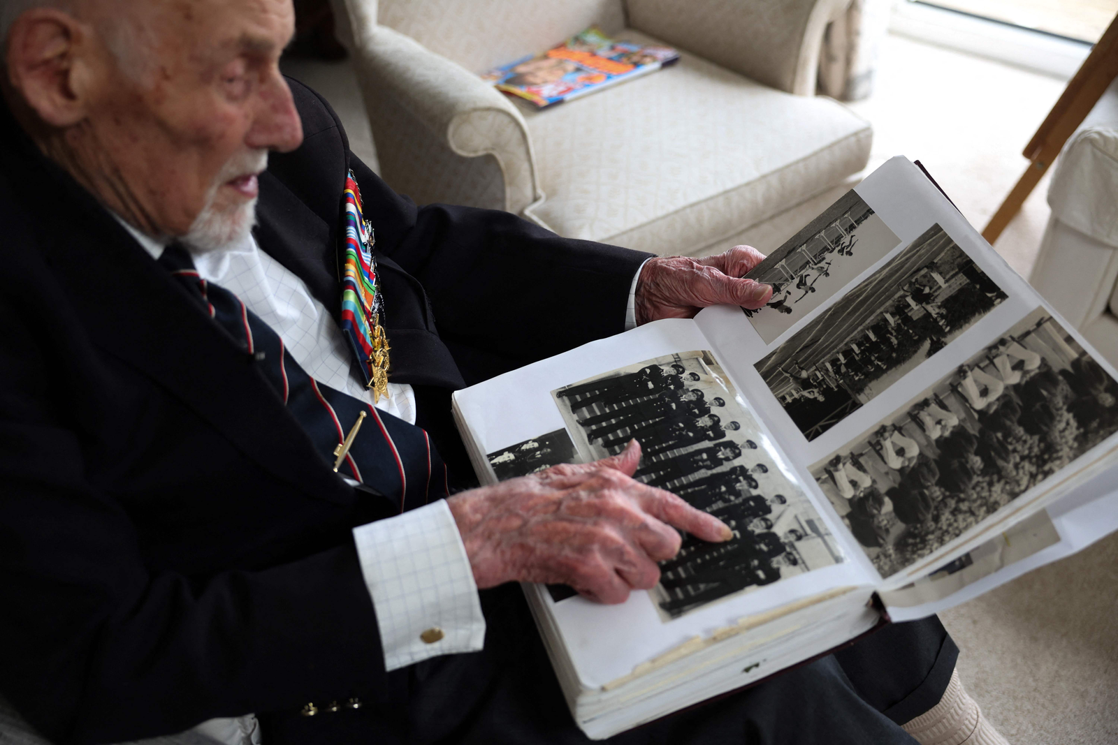 O ex-oficial da Marinha Real britânica e veterano do Dia D, contra-almirante John Roberts, olha um álbum de fotos contendo fotos de seu serviço durante a Segunda Guerra Mundial, na sala de sua casa em Whitstable, Kent — Foto: Daniel LEAL / AFP