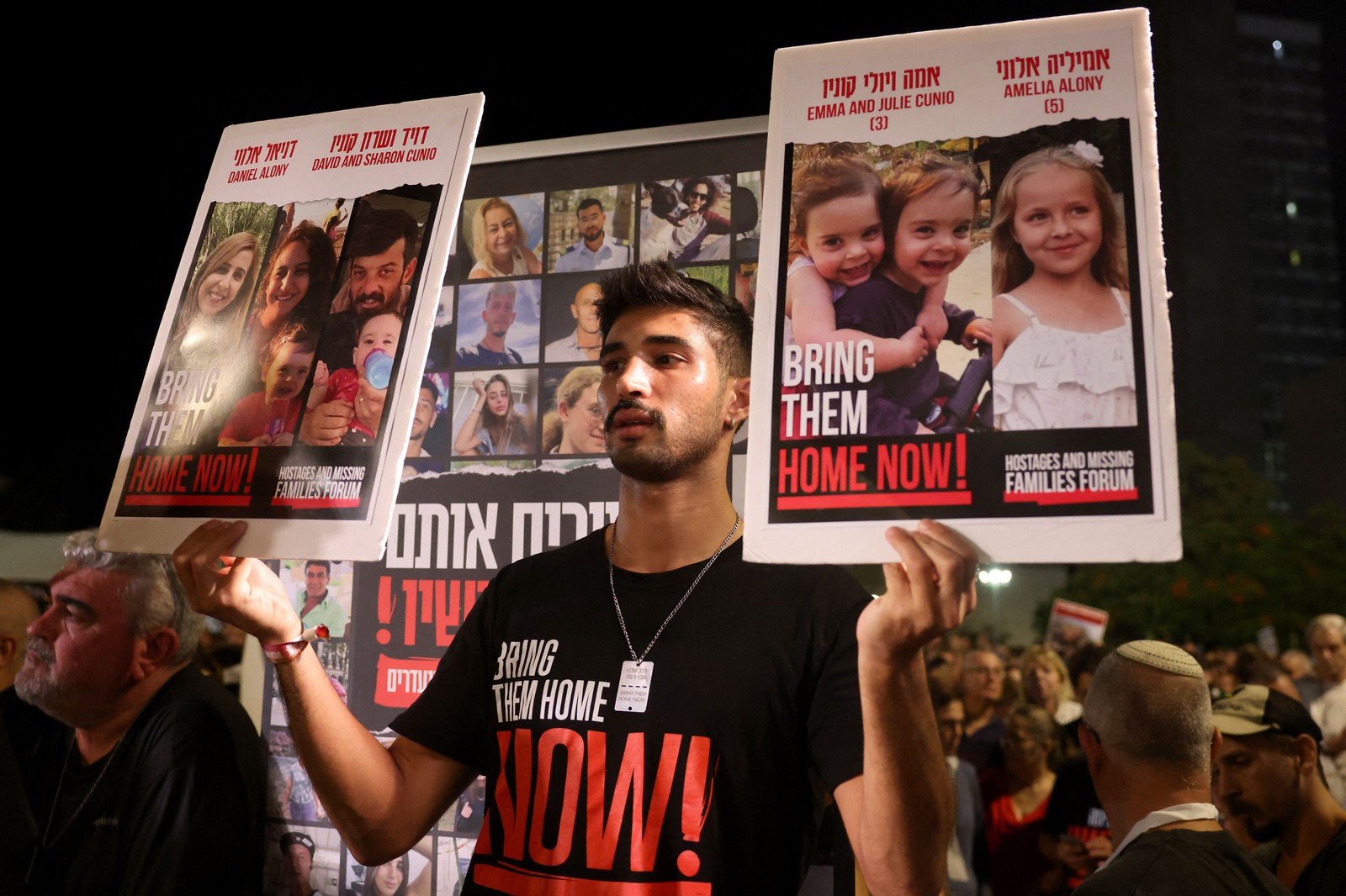 Homem segura retratos das reféns israelenses Emma e Julie Cunio ao lado de Amelia Alony (diretia), durante uma manifestação pedindo a libertação dos reféns israelenses sequestrados por militantes palestinos e atualmente detidos na Faixa de Gaza, em Tel Aviv, em 4 de novembro de 2023. — Foto: AHMAD GHARABLI / AFP