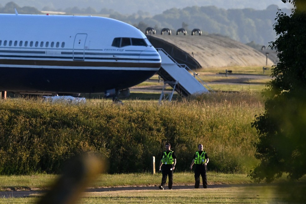 Policiais caminham perto de onde um Boeing 767 na pista da base militar de Amesbury, Salisbury, onde se preparava para enviar refugiados do Reino Unido para Ruanda — Foto: Justin Tallis / AFP