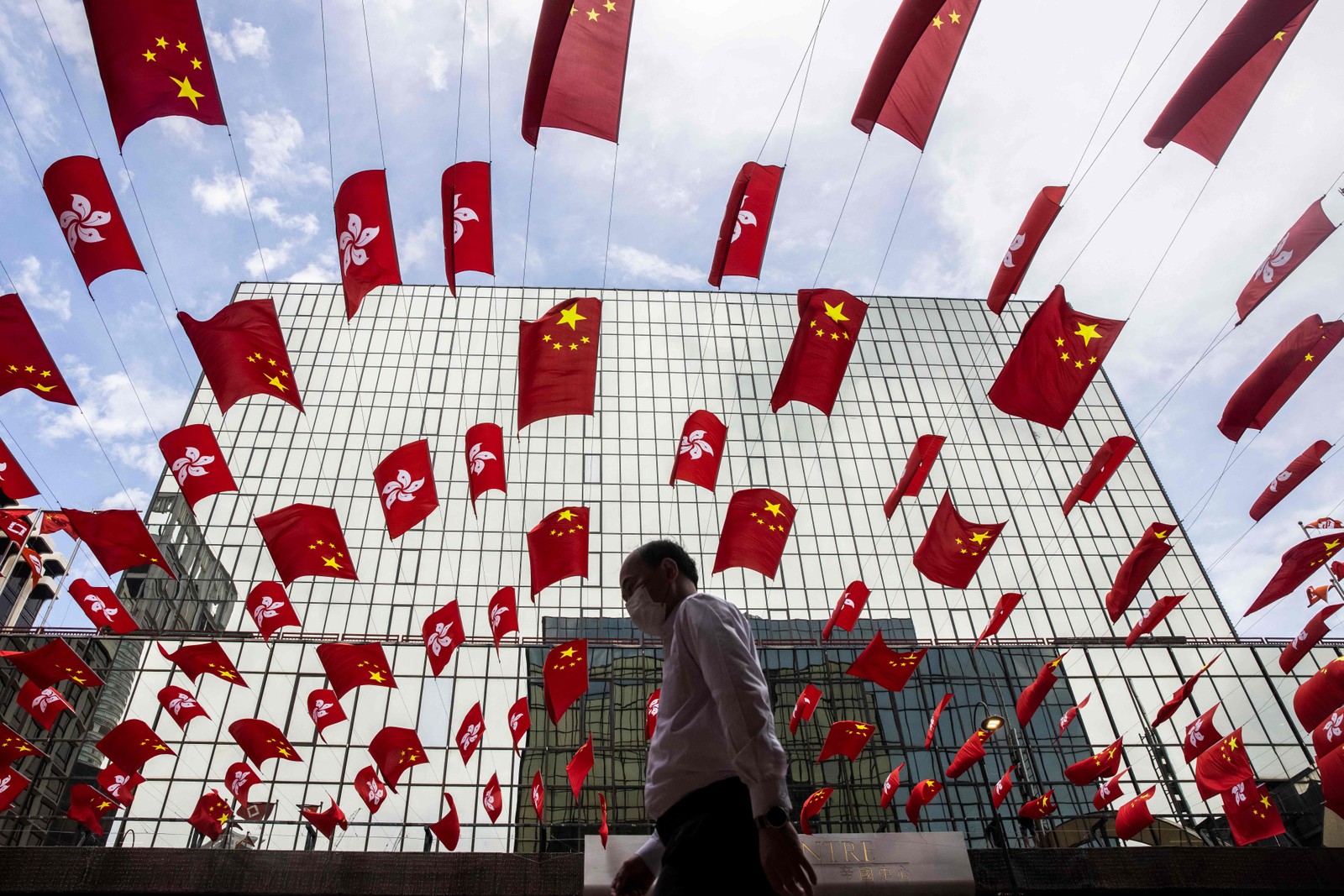 Homem caminha sob uma exibição das bandeiras de Hong Kong e da China no distrito de Tsim Sha Tsui, em Hong Kong — Foto: ISAAC LAWRENCE / AFP