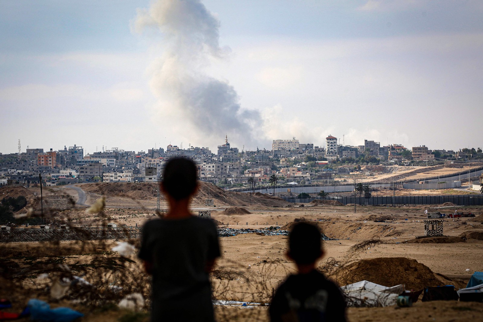 Crianças observam coluna de fumaça de bombardeio subindo em Rafah — Foto: AFP