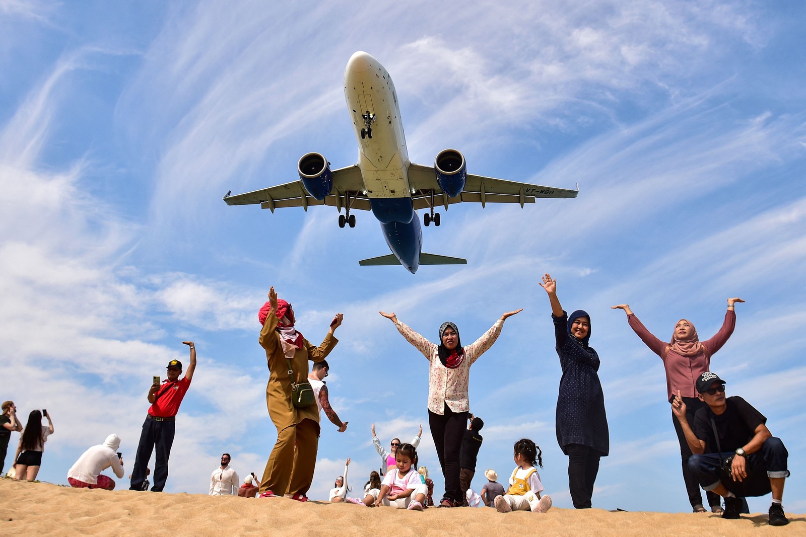 Turistas posam para foto na praia de Mai Khao quando um avião pousa no Aeroporto Internacional de Phuket — Foto: MADAREE TOHLALÁ/AFP