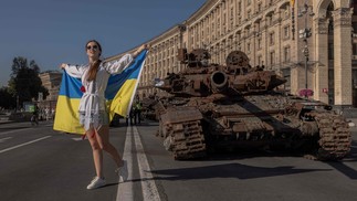 Mulher posa para fotos segurando a bandeira ucraniana ao lado de veículos militares russos destruídos em Kiev — Foto: Roman Pilipey / AFP