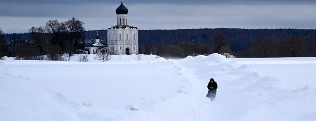 Mmulher caminha em um prado coberto de neve em frente ao Pokrova do século 12 na catedral ortodoxa de Nerli, fora da cidade de Vladimir, a cerca de 200 km de Moscou — Foto: KIRILL KUDRYAVTSEV/AFP