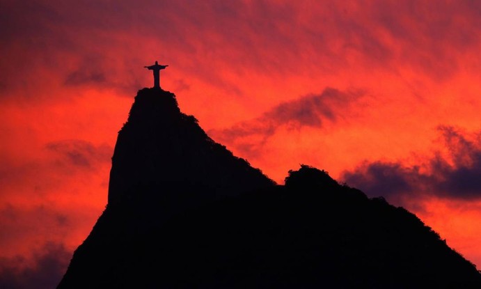 Silhueta do Corcovado, com o Cristo Redentor no topo. é vista em contraste com céu avermelhado de um pôr do sol em 2009