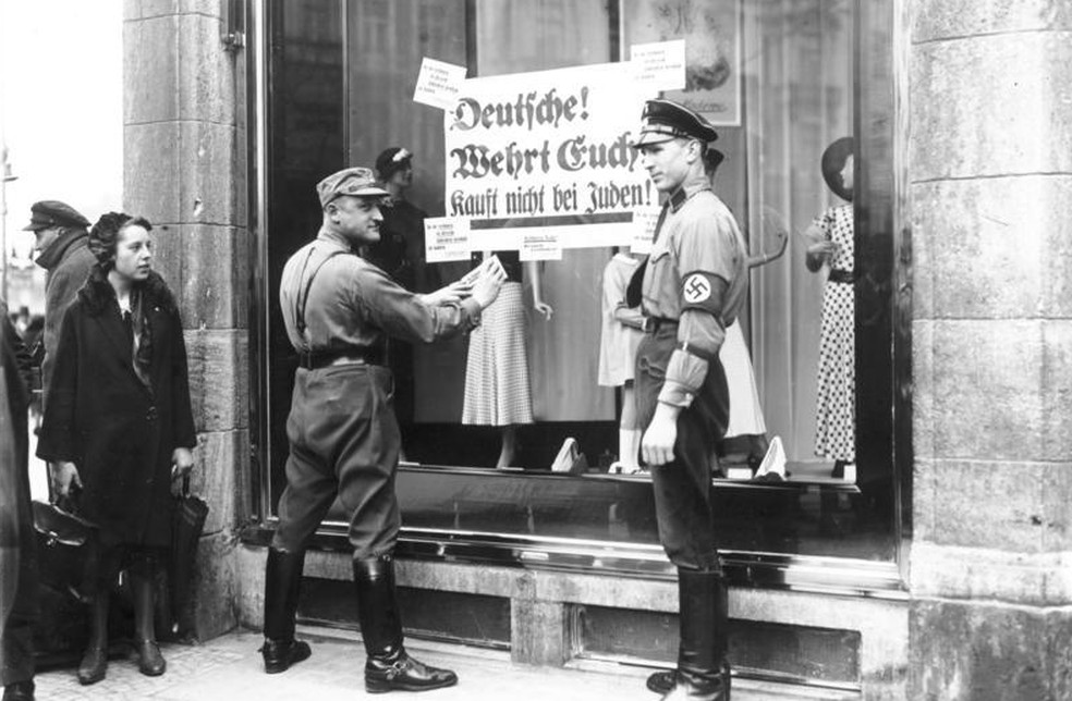 Soldados alemães prendem cartaz em loja de dono judeu: "Não comprem de judeus" — Foto: Reprodução/Arquivo Federal Alemão