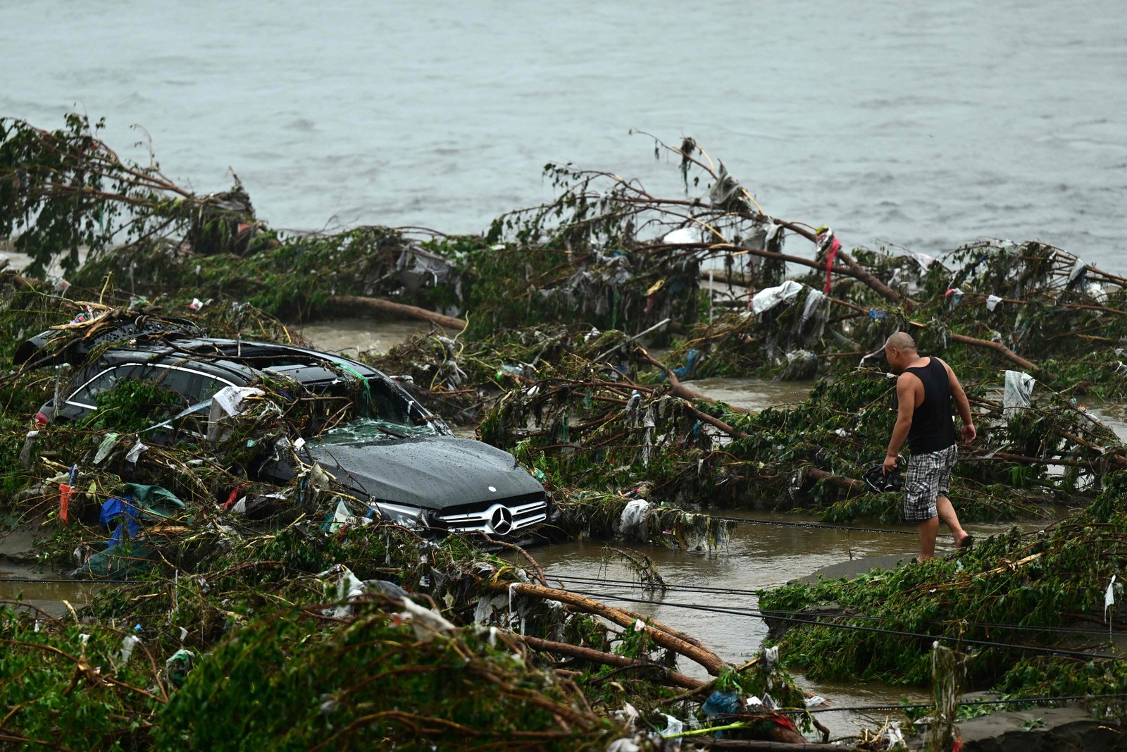 Homem olha para um carro danificado após fortes chuvas no distrito de Fangshan, em Pequim, em 1º de agosto de 2023 — Foto: Pedro PARDO / AFP