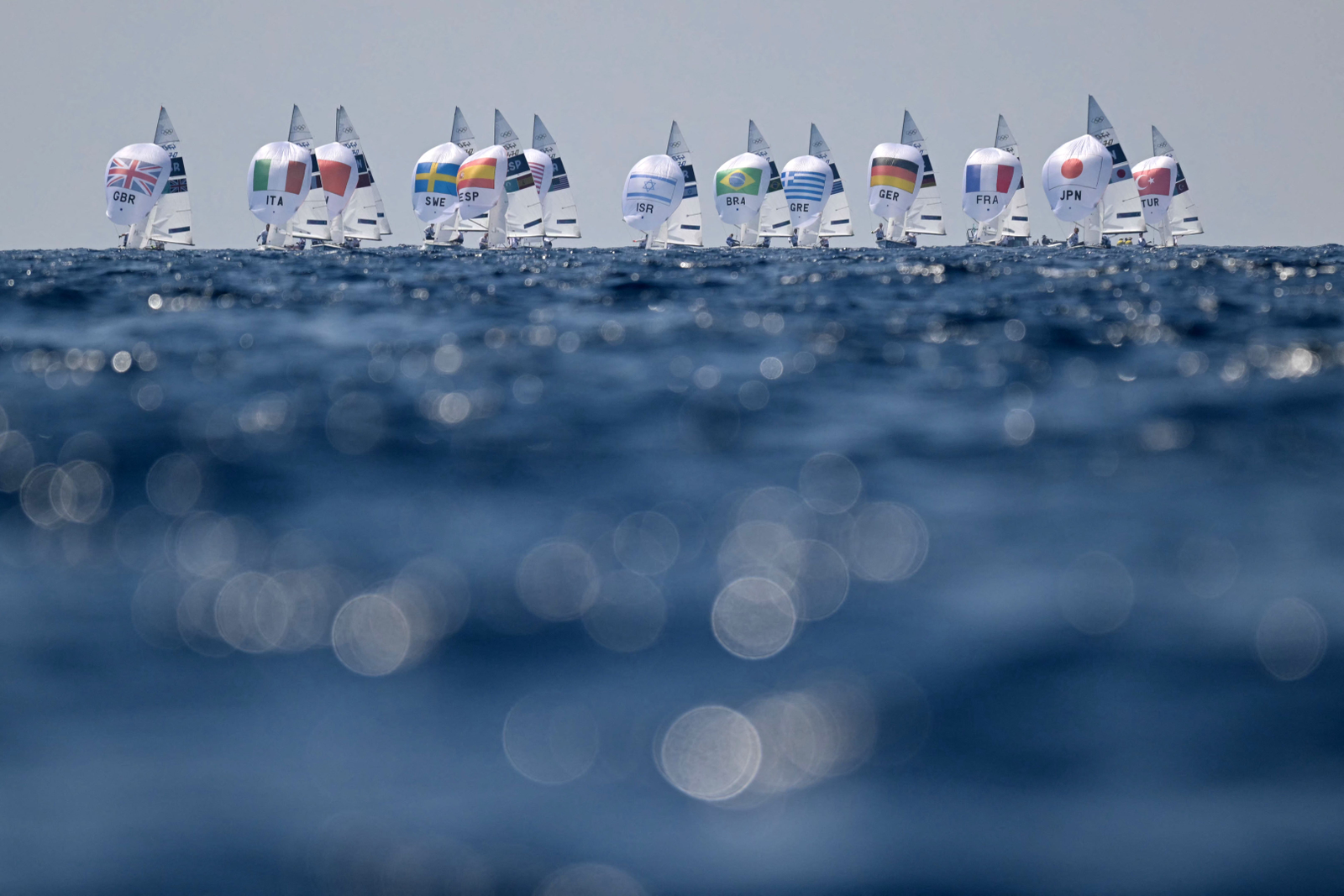 Equipes de vela alinhadas no horizonte durante os Jogos Olímpicos de Paris 2024 — Foto: Nicolas TUCAT / AFP