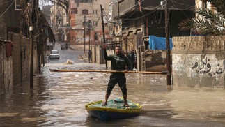 Palestino anda de prancha em uma rua inundada após fortes chuvas no campo de refugiados Al-Shati na Faixa de Gaza — Foto: MOHAMMED ABED/AFP