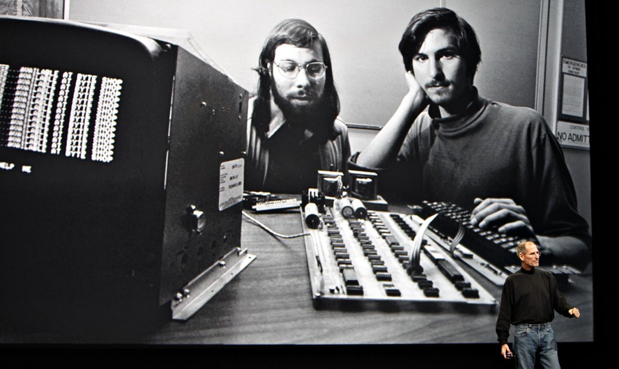 Steve Jobs em evento da Apple, com foto no telão ao fundo de quando era jovem, ao lado de seu amigo Steve Wozniak: os dois fundaram a Apple