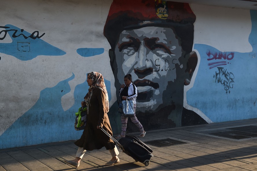 Mulher passa por imagem de Hugo Chávez em muro de Caracas