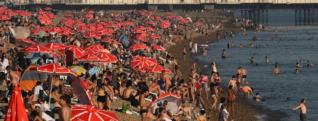 Banhistas são vistos aproveitando o sol e o mar na praia de Brighton — Foto: AFP