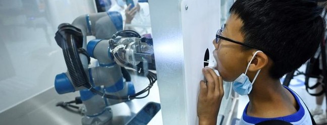 Menino faz um teste de PCR realizado por um simulação por um braço robótico durante a Conferência Mundial de Robôs, que acontece em Pequim, na China — Foto: WANG Zhao / AFP