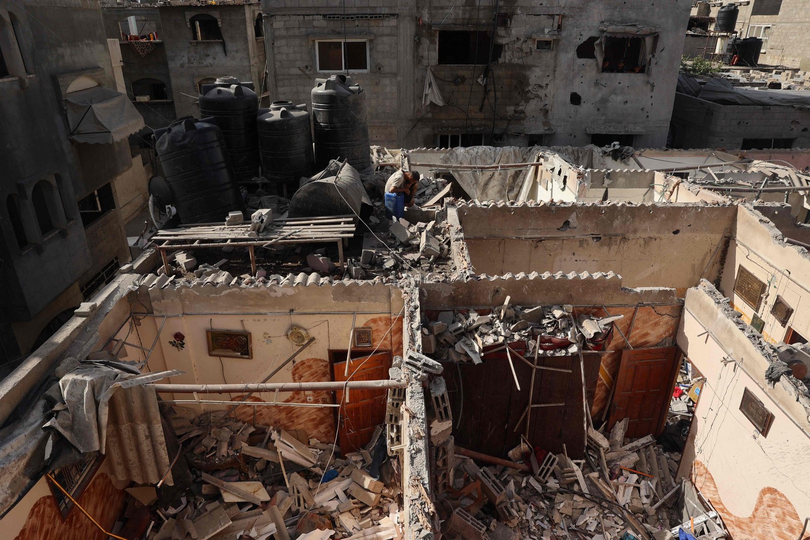 Um homem palestino descansa depois de encher um galão com água do telhado de uma casa fortemente danificada após o bombardeio israelense no distrito de Tal al-Sultan, em Rafah, no sul da Faixa de Gaza — Foto: AFP