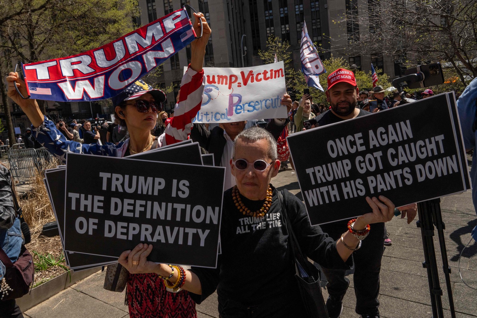Manifestantes pró-Trump e anti-Trump seguram cartazes fora do Tribunal Criminal de Manhattan enquanto o ex-presidente dos EUA, Donald Trump, comparece ao primeiro dia de seu julgamento — Foto: Adam Gray / AFP