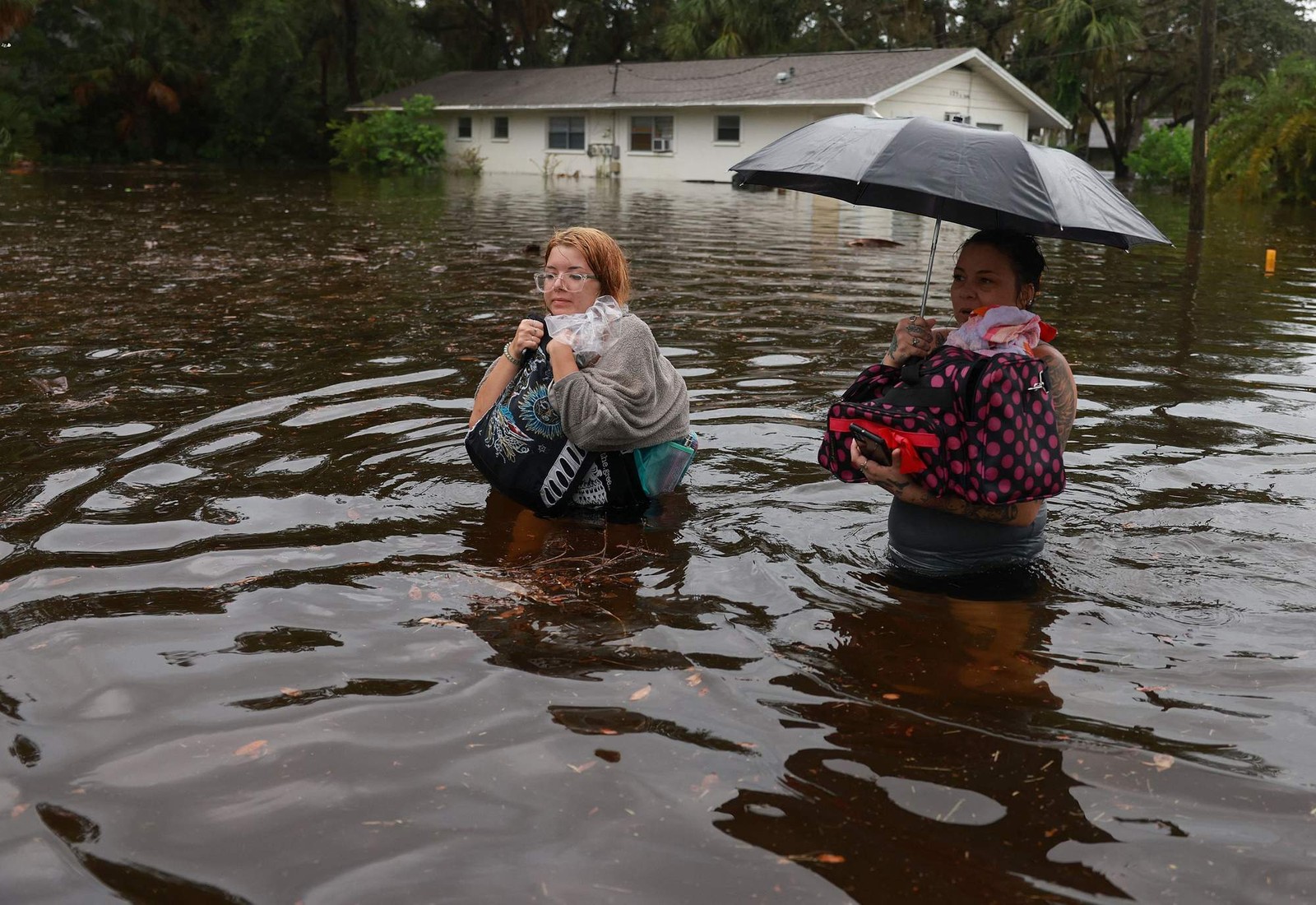 Makatla Ritchter (e) e sua mãe, Keiphra Line, atravessam as águas da enchente depois de terem que deixar sua casa quando as águas da enchente do furacão Idalia — Foto: JOE RAEDLE / GETTY IMAGES NORTH AMERICA / Getty Images via AFP