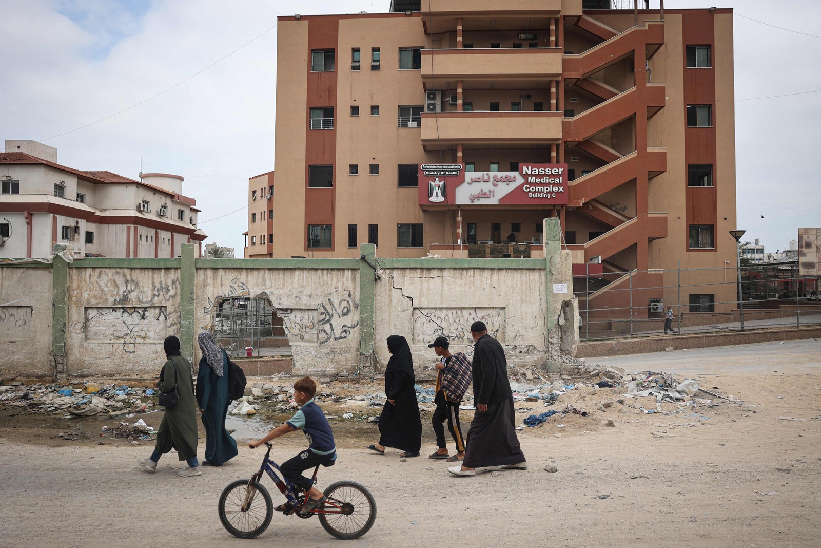 Palestinos passam pelo Hospital Nasser danificado em Khan Yunis, no sul da Faixa de Gaza, em 2 de maio de 2024, em meio ao conflito em curso entre Israel e o grupo militante palestino Hamas. — Foto: AFP