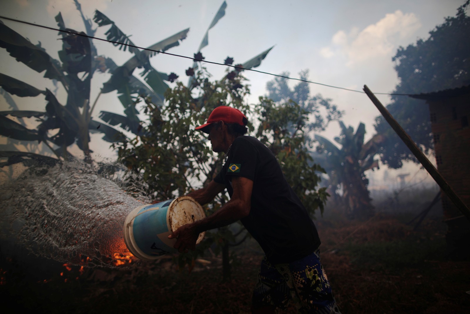 Rosalino de Oliveira joga água tentando proteger sua casa enquanto o fogo se aproxima em uma área da floresta amazônica, perto de Porto Velho, RondôniaREUTERS