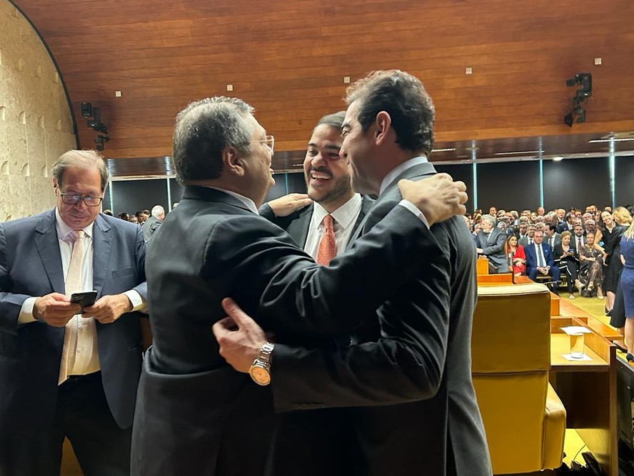 Os ministros Flávio Dino (Justiça) e Jorge Messias (AGU) e o presidente do TCU, Bruno Dantas, se abraçam na posse de Luís Roberto Barroso na presidência do STF; os três miram a vaga de Rosa Weber
