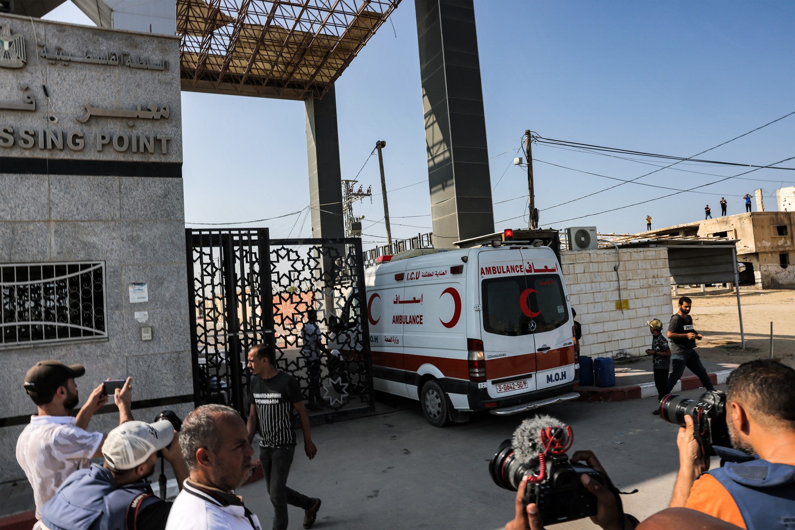 Jornalistas filmam enquanto uma ambulância do Ministério da Saúde palestino atravessa o portão para entrar na passagem de fronteira de Rafah, no sul da Faixa de Gaza, antes de cruzar para o Egito — Foto: Mohammed ABED/AFP