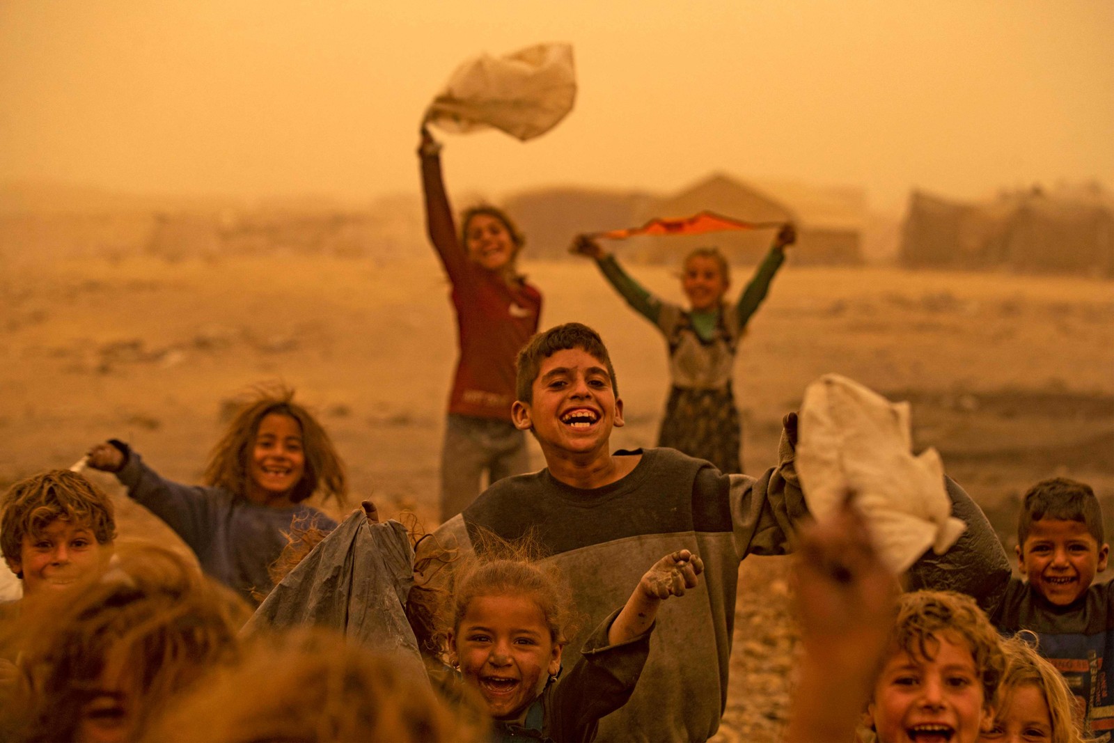 Crianças brincam em meio a uma tempestade de areia no campo Sahlah al-Banat para deslocados no interior de Raqa, no norte da Síria  — Foto: DELIL SOULEIMAN / AFP