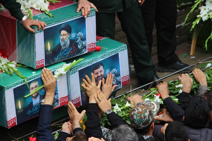 Pessoas participam de um cortejo fúnebre ao lado de um caminhão que transporta os caixões do presidente Ebrahim Raisi e seus sete assessores em Tabriz, província do Azerbaijão Oriental, em 21 de maio de 2024.