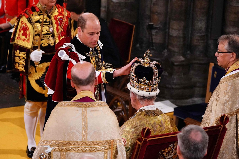 O príncipe William, príncipe de Gales, toca a coroa de Santo Eduardo na cabeça de seu pai, o rei Charles III — Foto: Yui Mok / POOL / AFP