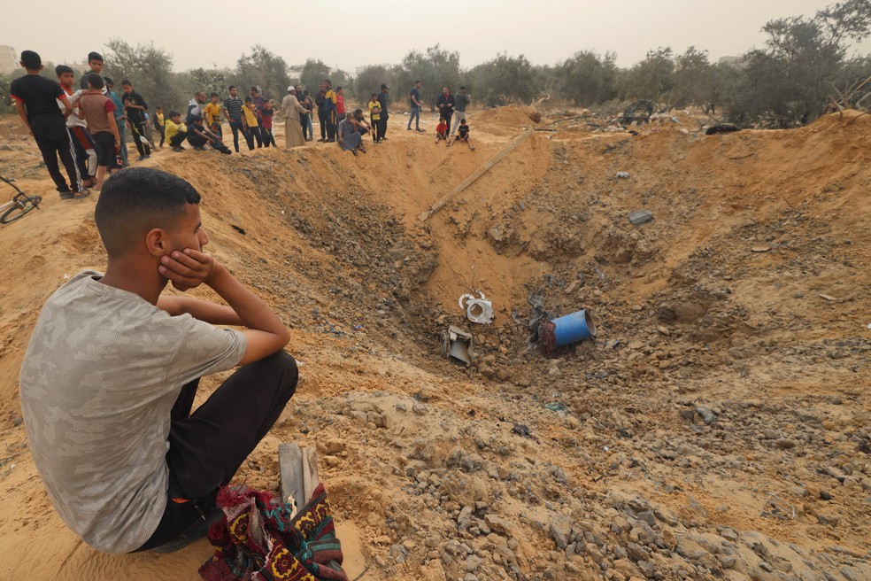 Palestinos se reúnem em torno de uma enorme cratera após um bombardeio israelense durante em Rafah. — Foto: MOHAMMED ABED / AFP