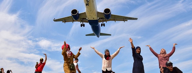 Turistas posam para foto na praia de Mai Khao quando um avião pousa no Aeroporto Internacional de Phuket — Foto: MADAREE TOHLALÁ/AFP