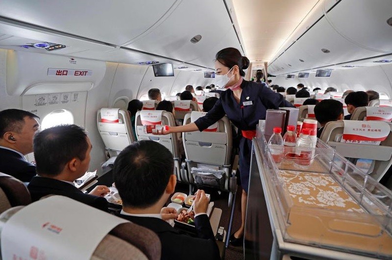 Aeromoça serve a refeição aos passageiros do primeiro voo comercial do C919, avião chinês que almeja rivalizar com Boeing e Airbus — Foto: AFP