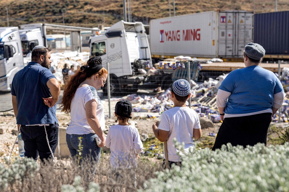 Colonos israelenses observam carga humanitária destinada a Gaza espalhada por estrada na Cisjordânia — Foto: Oren ZIV / AFP