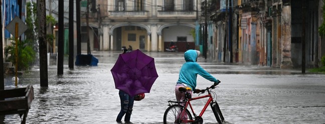 Pessoas caminham por uma rua inundada em Havana, durante a passagem da tempestade tropical Idalia. — Foto: Yamil LAGE/AFP