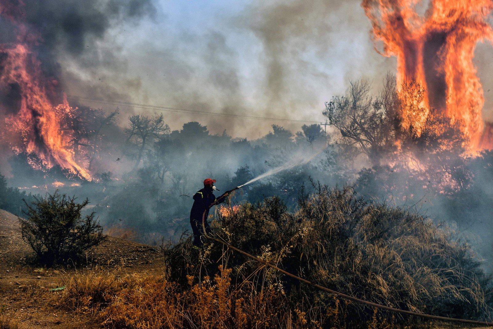 Um bombeiro tenta conter incêndio na área de Agioi Theodori, próximo à Atenas, na Grécia. As autoridades de saúde soaram alarmes da América do Norte à Europa e Ásia, pedindo às pessoas que se mantenham hidratadas e protegidas do sol escaldante, em um lembrete dos efeitos do aquecimento global. — Foto: Valerie GACHE / AFP