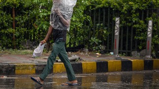 Pedestre usa um saco plástico para se cobrir durante uma chuva torrencial em Jalandhar, Índia — Foto: SHAMMI MEHRA/AFP