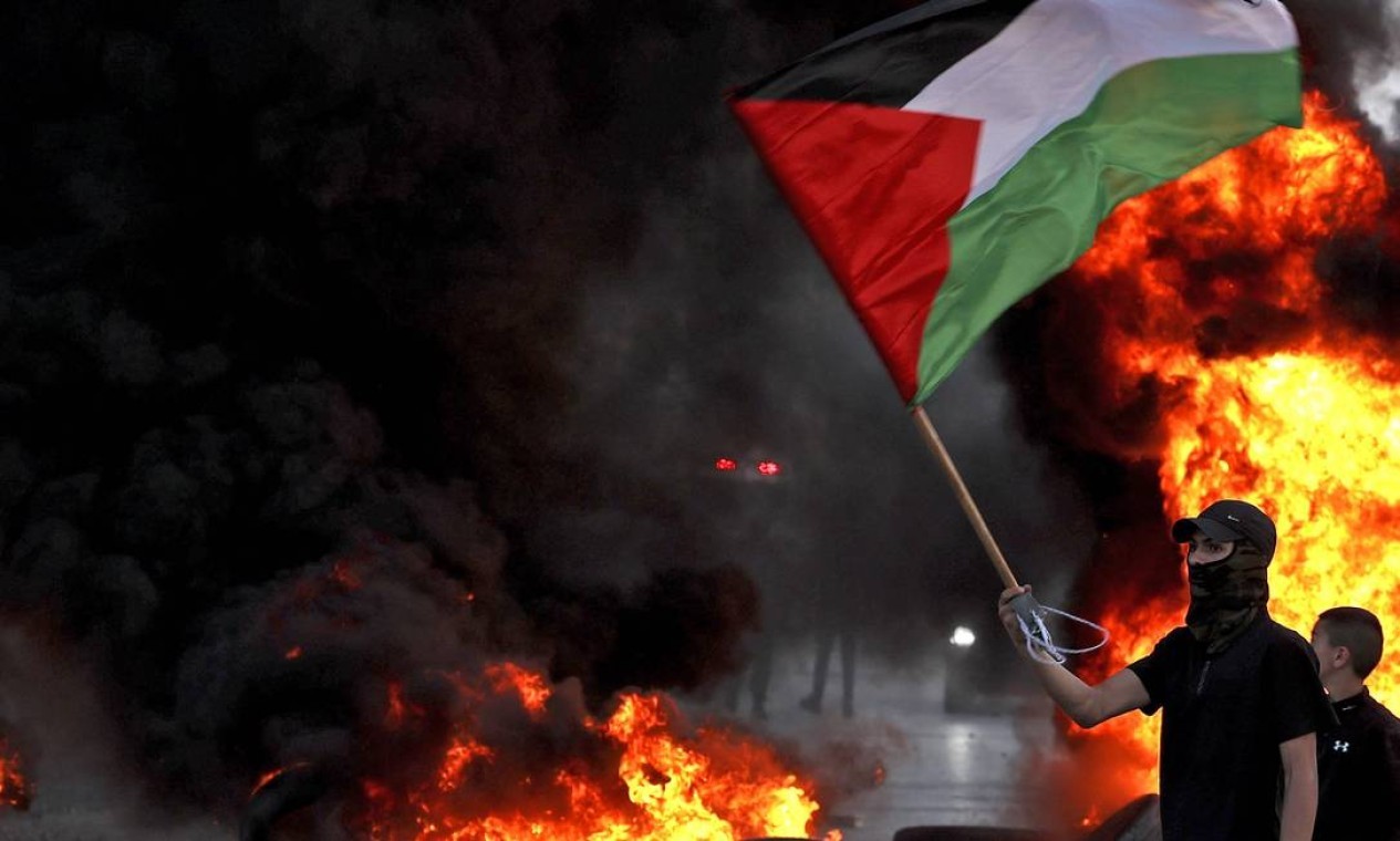 manifestante mascarado agita uma bandeira palestina perto de barricada em chamas durante confrontos com as forças israelenses após protesto para denunciar a "marcha da bandeira" nacionalista – lê-se extremista — Foto: ABBAS MOMANI / AFP
