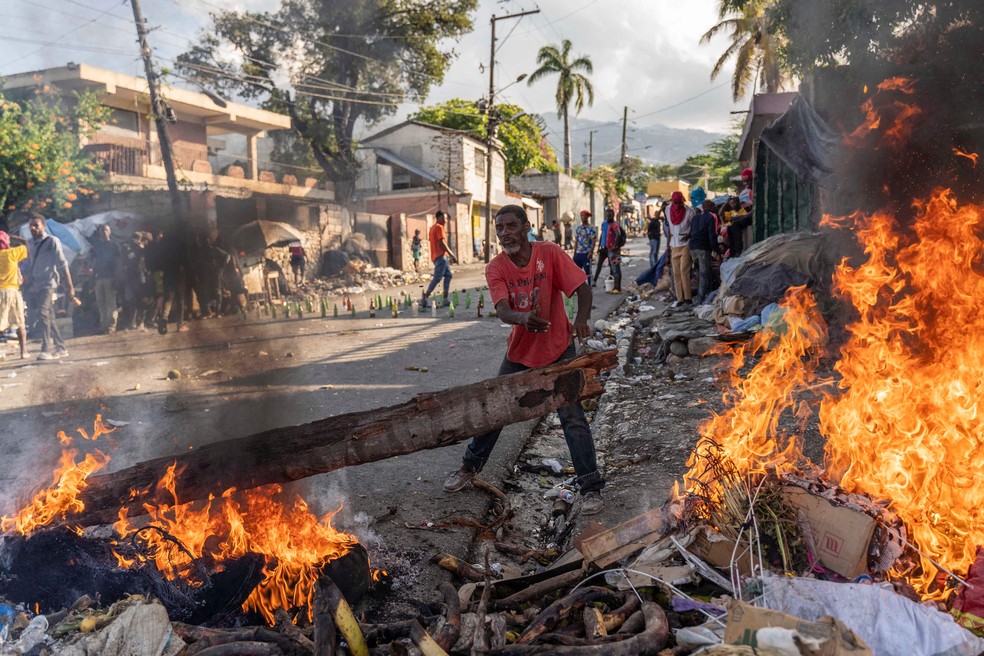 Homem joga lenha em barricada durante protesto exigindo a renúncia do primeiro-ministro Ariel Henry, na área de Petion-Ville, em Porto Príncipe, Haiti — Foto: RICHARD PIERRIN / AFP