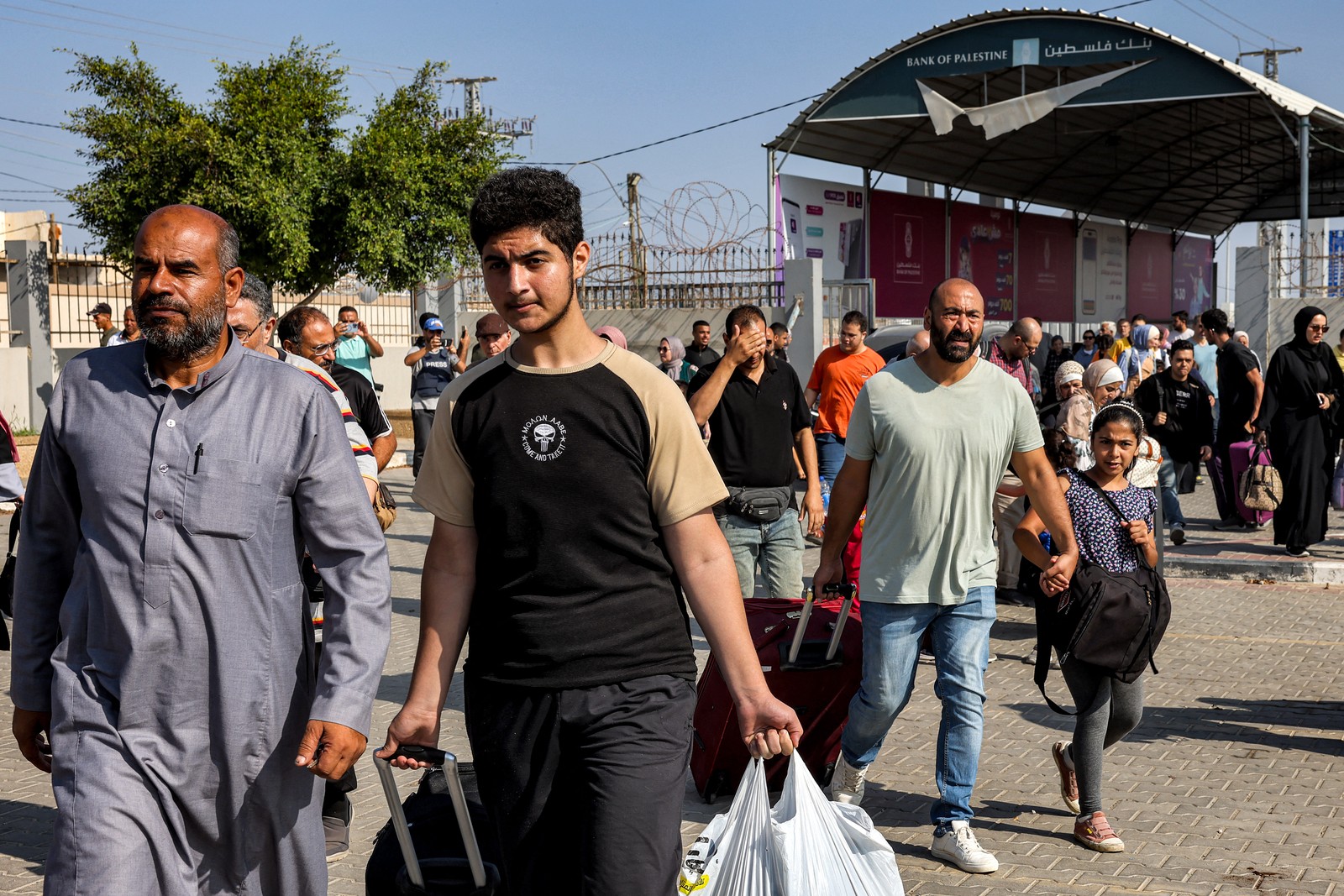 Pessoas atravessam um portão para entrar na passagem de fronteira de Rafah para o Egito, no sul da Faixa de Gaz — Foto: Mohammed ABED/AFP