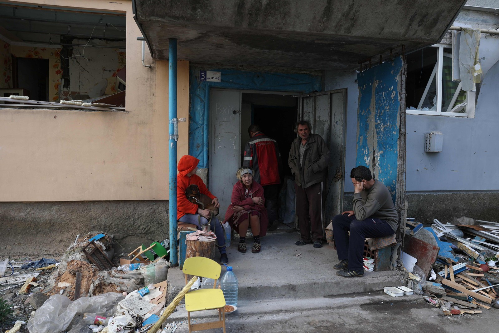 Moradores locais sentam-se na entrada de um prédio de apartamentos destruído por bombardeio em Ocheretyne — Foto: Anatolii STEPANOV/AFP