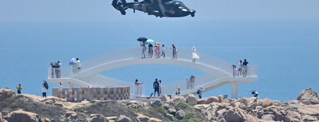 Turistas presenciam helicópteros militares chineses sobrevoam a Ilha de Pingtan, na província de Fujian, um dos pontos do litoral chinês mais próximos de Taiwan — Foto: HECTOR RETAMAL / AFP