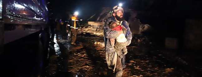 Membro da defesa civil síria carrega uma criança resgatada dos escombros após um terremoto na cidade de Zardana, no interior da província de Idlib, noroeste da Síria — Foto: Abdulaziz KETAZ / AFP