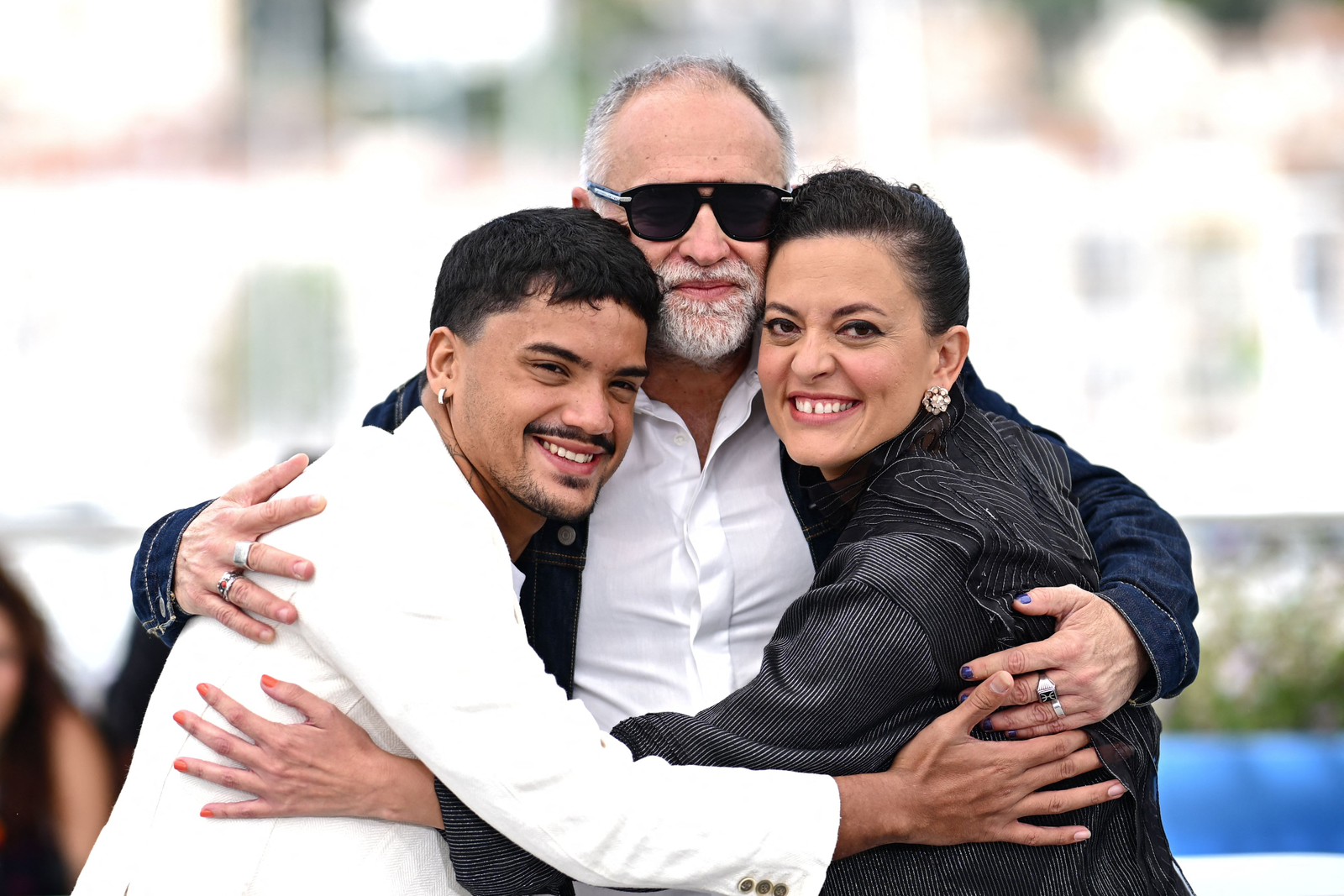 Iago Xavier e Nataly Rocha abraçando o diretor Karim Ainouz. — Foto: LOIC VENANCE / AFP