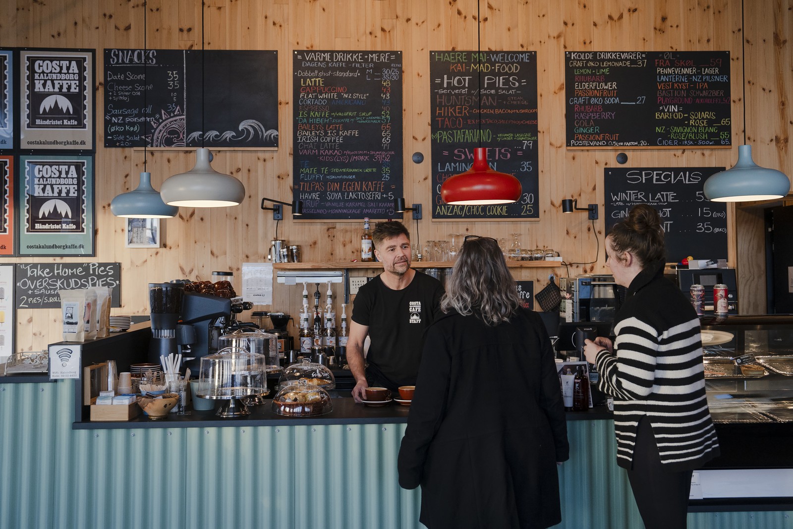 Shaun Gamble e os clientes do café Costa Kalundborg Kaffe, com vista para o porto em Kalundborg — Foto: Charlotte de la Fuente/The New York Times