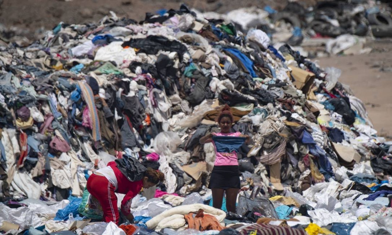 Mulheres buscam roupas em meio a toneladas descartadas no deserto do Atacama  — Foto: MARTIN BERNETTI / AFP