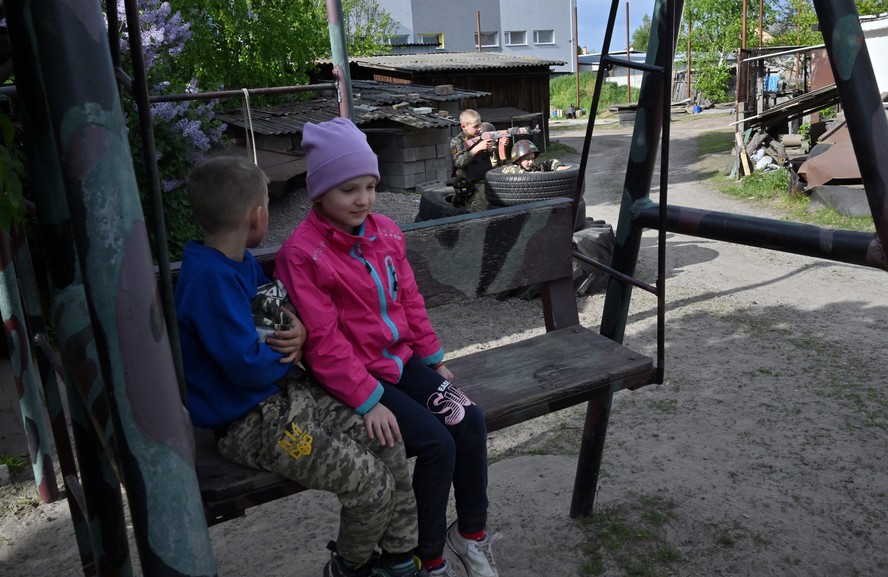 Crianças conversam em parque enquanto outra 'brinca' de guerra, nos arredores de Kiev