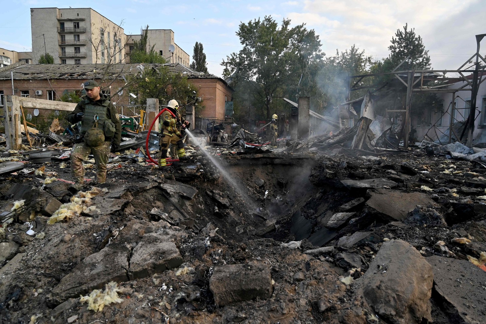 Bombeiros apagam um incêndio enquanto especialistas da polícia procuram fragmentos de mísseis em uma área industrial da capital ucraniana, Kiev — Foto: Sergei SUPINSKY/AFP