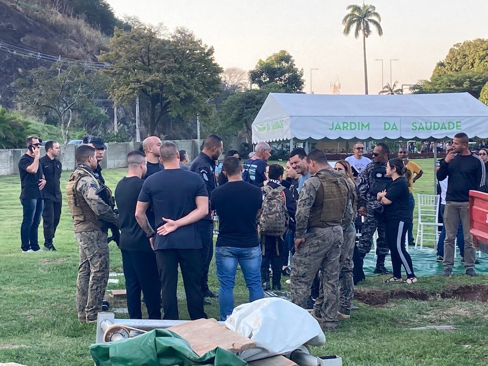 Enrolado numa bandeira do Bope e com uma mochila do batalhão nas costas, filho do PM Jorge Henrique Galdino Cruz recebe as condolências no enterro do pai — Foto: Camila Araujo